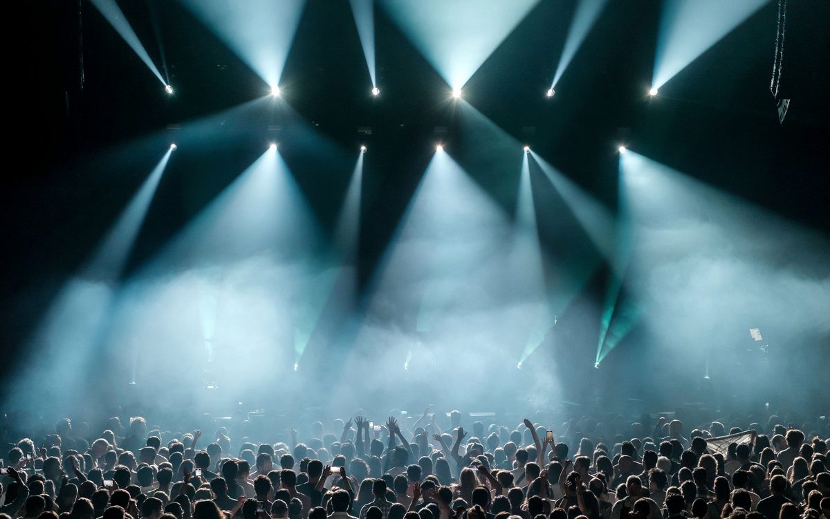 Concert crowd under stage lights at a large indoor music event