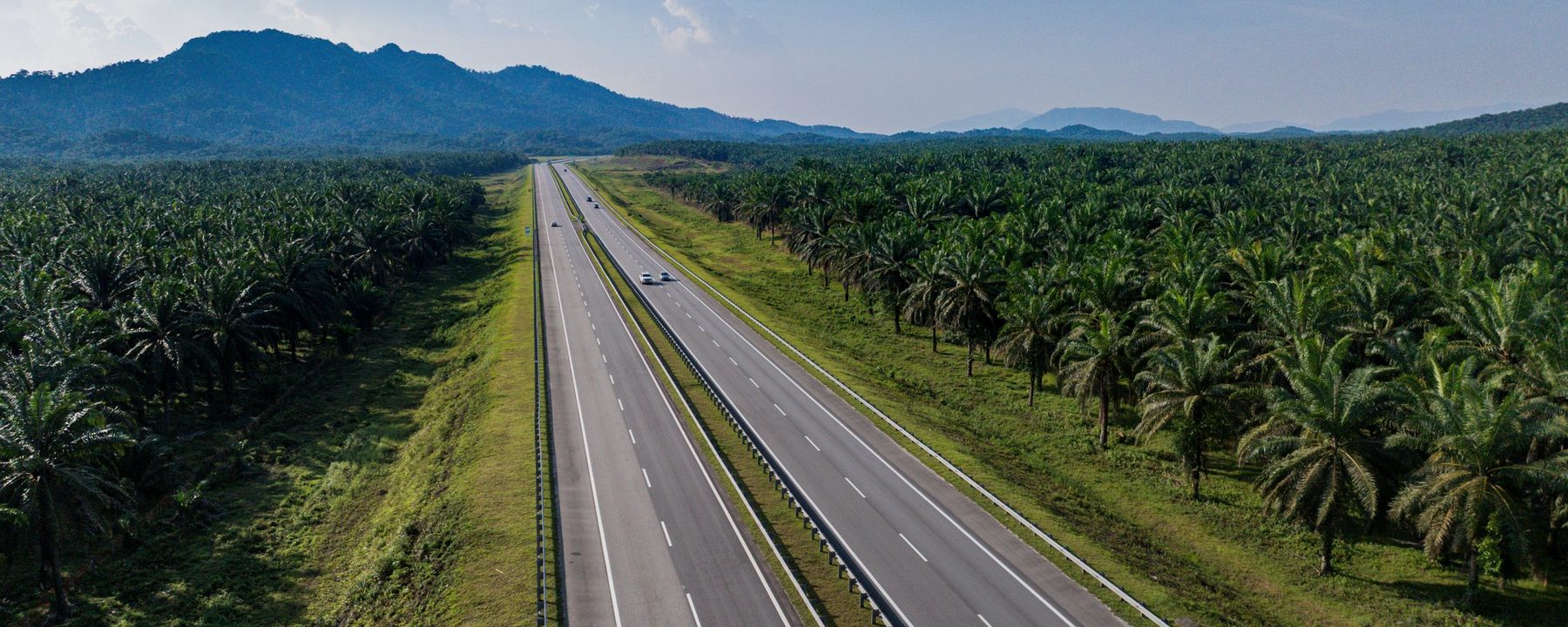 Malaysian expressway running between oil palm plantations towards distant hills